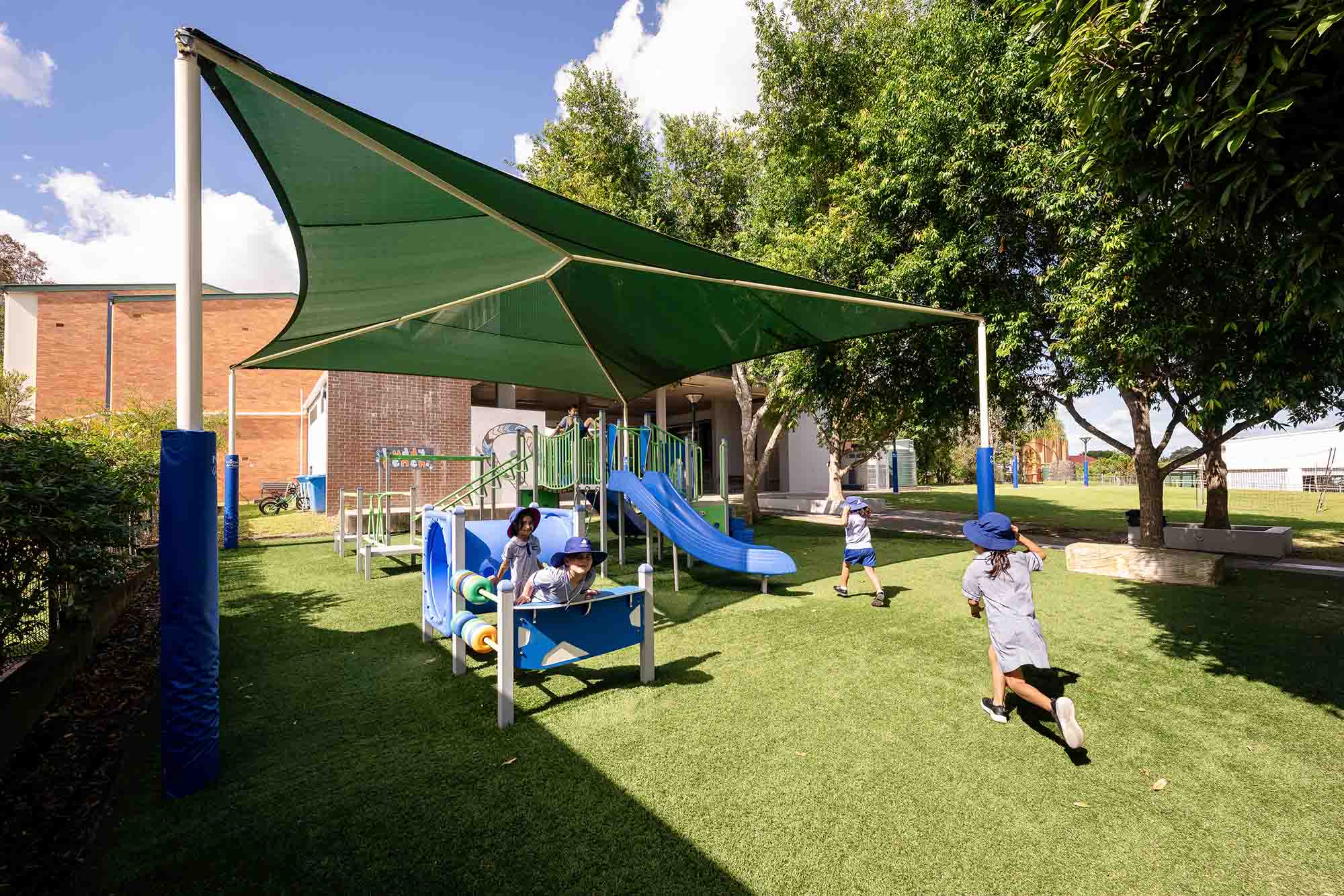 Students playing on outdoor playground equipment under shade structure in school yard