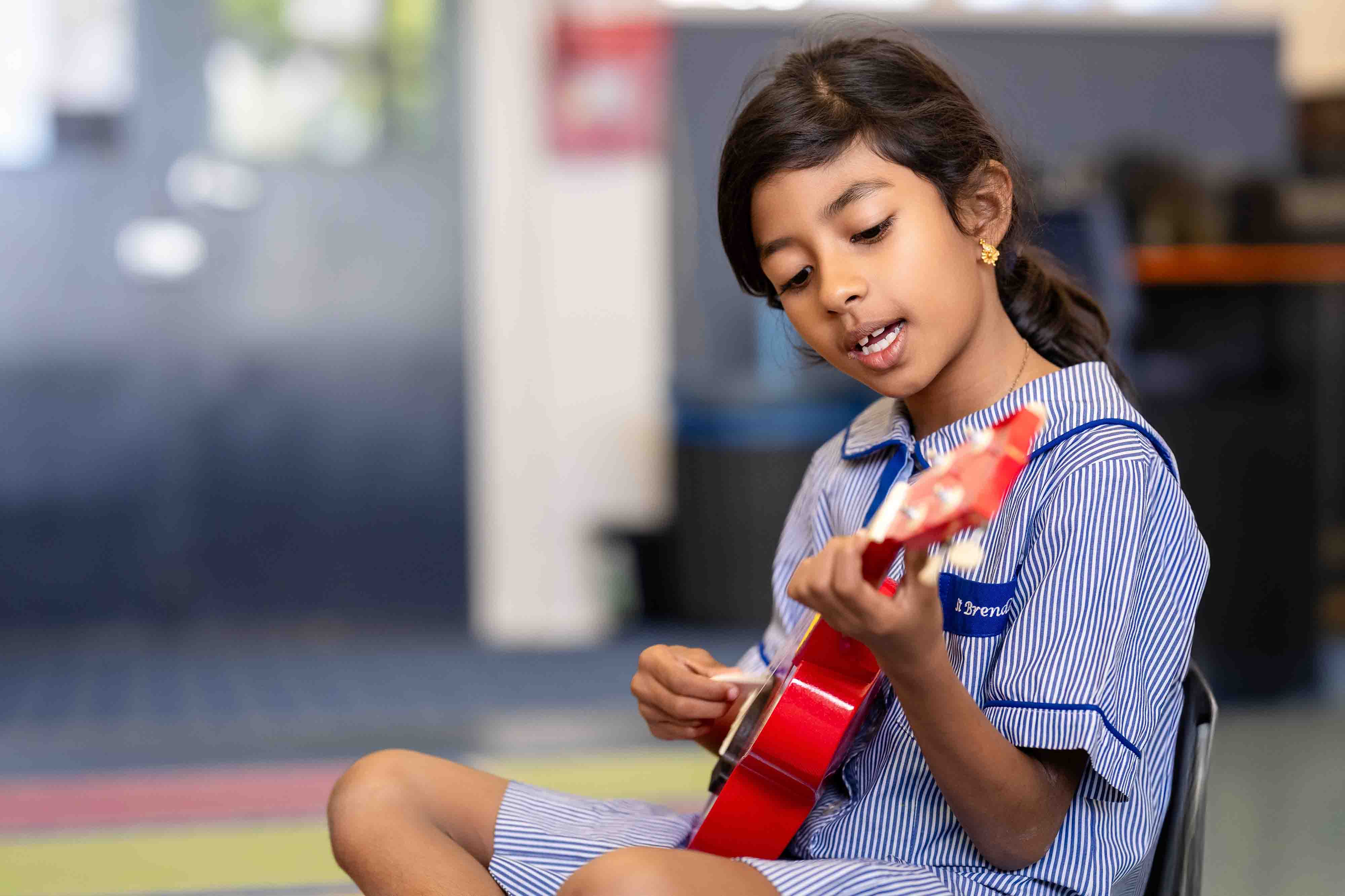 Student playing red ukulele during classroom music lesson