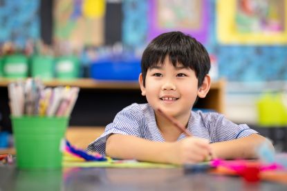Student smiling while working on creative classroom activity with colourful craft materials